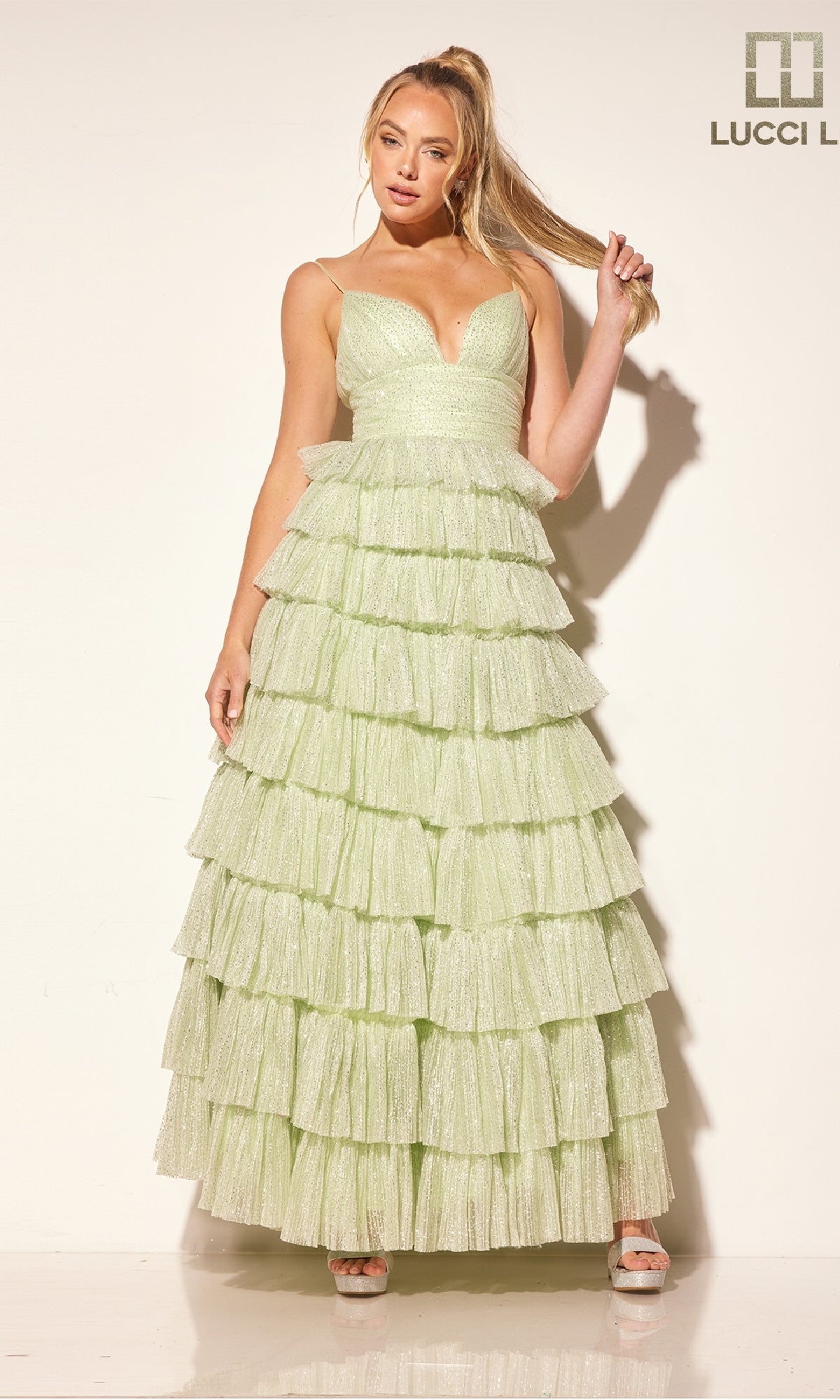 A woman poses against a plain background in the Lucci Lu 1342 Glitter Tulle Ruffle Prom Dress, featuring light green tiers, delicate straps, and a flowing ruffled skirt.